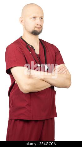 Un médecin chauve avec une barbe, portant des gommages rouges et un stéthoscope autour du cou, se tient debout les bras croisés. Banque D'Images