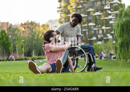 Deux amis, l’un avec une prothèse de jambe et l’autre en fauteuil roulant, partageant un moment de connexion et de soutien mutuel dans un parc urbain verdoyant. Le Banque D'Images