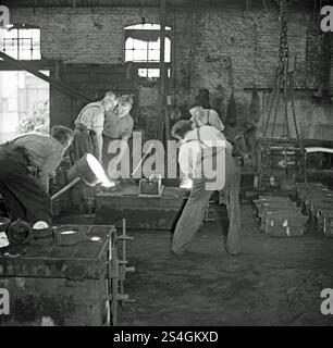 Ouvriers versant du métal fondu d'un creuset dans un moule (moule) dans un atelier de fonderie britannique vers 1930. Ce travail chaud et lourd est exigeant en main-d'œuvre et est encore souvent fait à la main. La coulée au sable, également connue sous le nom de coulée moulée au sable, est un procédé de coulée de métal caractérisé par l'utilisation de sable comme matériau de moulage. Les moulages en sable sont produits dans des usines spécialisées appelées fonderies. Le sable est généralement contenu dans un ensemble de cadres ou de boîtes de moule connu sous le nom de flacon. Les moules en sable sont une forme de moulage relativement bon marché. Banque D'Images