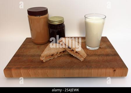 Sandwich au beurre d'arachide et à la gelée, étant fait sur une planche à découper devant un fond blanc Banque D'Images