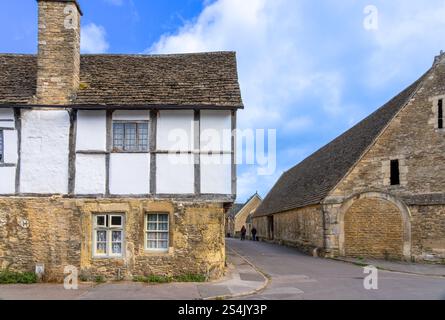 Lacock Royaume-Uni - 9 août 2024 ; couple en distance chiens marchant entre bâtiments médiévaux patrimoniaux en pierre et en bois avec toit en ardoise Banque D'Images