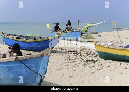 Kovalam, Malabar Coast, Malabar, Kerala, Inde du Sud, plusieurs bateaux de pêche avec des gens assis sur le rivage dans la mer calme, impressions de l'Inde du Sud Banque D'Images