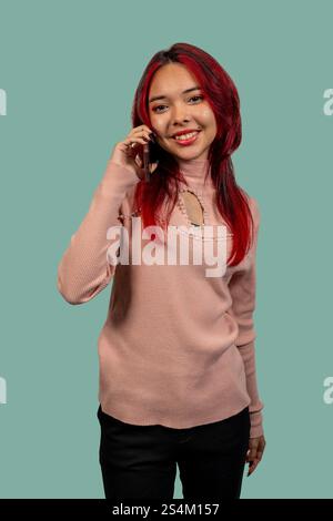 Photo studio d'une jeune femme aux cheveux roux utilisant un smartphone, souriant et regardant la caméra Banque D'Images