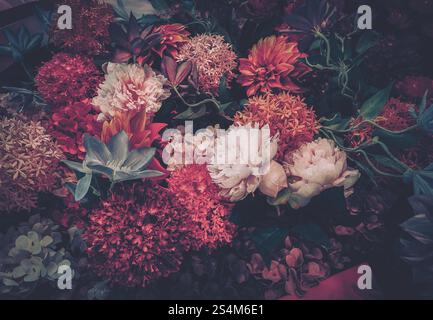Une image de style vintage mettant en valeur un arrangement luxuriant de fleurs artificielles, principalement dans des rouges et roses profonds. La composition suggère une célébration Banque D'Images