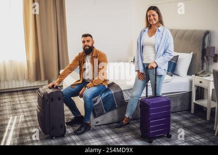 Jeune couple heureux est en vacances. Les touristes sont arrivés en chambre d'hôtel avec leurs valises. Banque D'Images