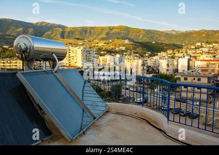 Un réservoir de chauffage de l'eau à énergie solaire sur le toit plat d'un immeuble d'appartements à Himare sur la Riviera albanaise. Les panneaux photovoltaïques. Banque D'Images