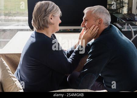 Un moment intime entre un couple aîné, assis étroitement et souriant l'un à l'autre la chaleur et l'affection entre eux créent un atmo confortable et aimant Banque D'Images