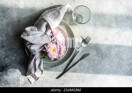 Une table élégante avec des chrysanthèmes roses sur une assiette grise, accompagnés d'une serviette en lin et de couverts en acier inoxydable, créant un a serein Banque D'Images