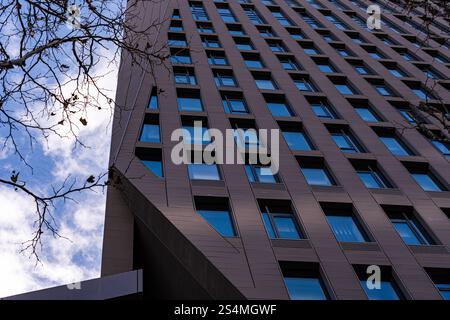 Photo à angle bas d'un gratte-ciel moderne haut placé contre un ciel bleu, avec des rangées de fenêtres et des panneaux architecturaux détaillés. Banque D'Images