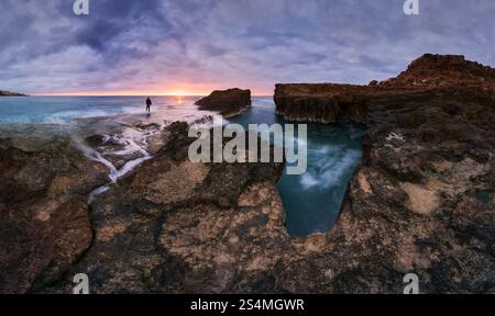 Lever de soleil captivant sur le rivage rocheux à Cabo Cervera à Torrevieja, Alicante, Espagne Une figure solitaire se dresse contre le ciel vibrant, entouré par se Banque D'Images