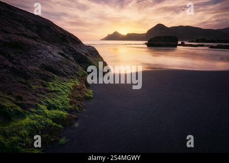 Le coucher de soleil tranquille jette une teinte dorée sur les rochers escarpés et les eaux calmes de Cala del Lastre à Murcie, en Espagne, créant une côte paisible et pittoresque Banque D'Images
