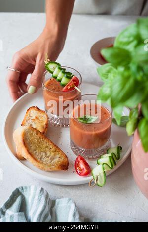 Un repas d'été rafraîchissant avec gazpacho frais garni de concombre, tomate et basilic, accompagné de pain grillé croustillant, serti sur une assiette blanche Banque D'Images