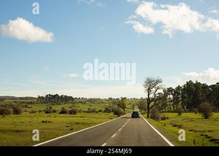Une voiture voyage le long d'une route de campagne tranquille sous un ciel bleu clair par un matin d'automne paisible le paysage présente des champs verdoyants et éparpillés tr Banque D'Images