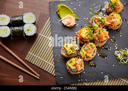 Vue de dessus de rouleaux de sushi assortis sur une planche d'ardoise sombre. Comprend des rouleaux classiques et des rouleaux embellissés avec des garnitures colorées. Banque D'Images