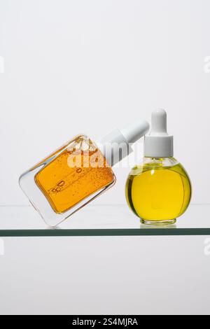 Deux élégants flacons de pipette remplis de sérum de vitamine C sont présentés sur une surface en verre mettant en valeur le liquide vibrant et translucide, idéal pour Beaut Banque D'Images