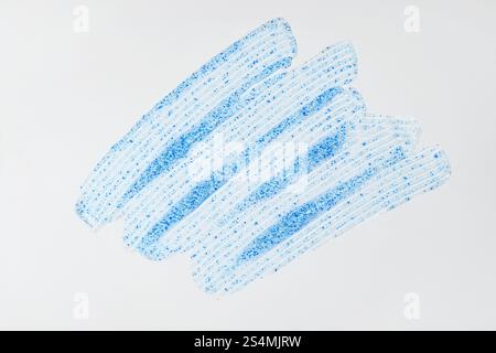 Étalement de gommage visage avec des particules micro-exfoliantes bleues sur fond blanc gros plan de texture crémeuse, idéal pour les thèmes de soin de la peau et de beauté Banque D'Images
