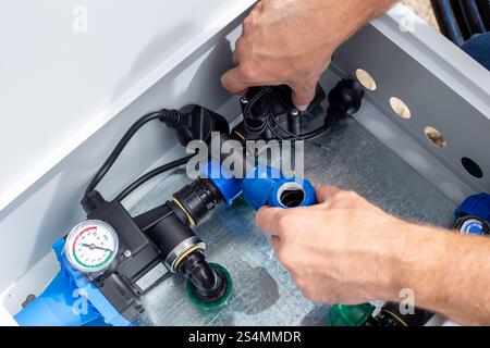 Un homme installe un système d'irrigation goutte à goutte en plaçant une valve automatique dans une boîte métallique. Banque D'Images