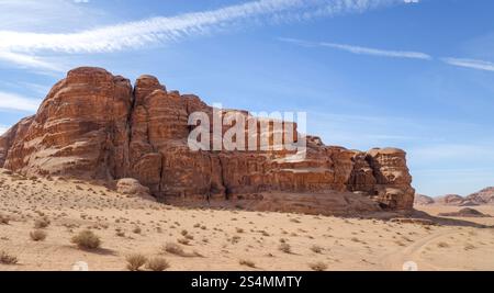 De majestueuses falaises de grès se dressent en bonne place dans le Wadi Rum, en Jordanie, sous un ciel bleu clair, mettant en valeur la beauté du désert et les merveilles géologiques. Banque D'Images