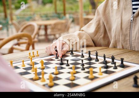 Une vue rapprochée d'une partie d'échecs jouée à l'extérieur sur une table en bois L'échiquier est décoré de pièces noires et blanches, entourées d'un su détendu Banque D'Images