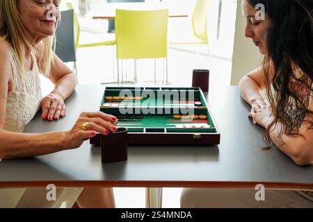 Mère et fille profiter d'un jeu de backgammon tranquille dans un café moderne la planche, avec son design classique, est posée sur une table élégante, capturant un moment Banque D'Images