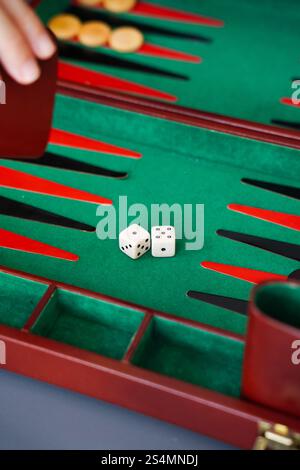 Gros plan d'un jeu de backgammon avec des dés sur un plateau vert Une main tient le cube doublant, améliorant l'aspect stratégique du jeu idéal pour le jeu de plateau en Banque D'Images