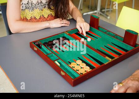 Un gros plan de deux personnes engagées dans un jeu de backgammon une personne déplace une pièce sur un tableau vert et rouge, créant une atmosphère confortable et stratégique Banque D'Images