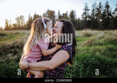 Portrait expressif mignon de mère embrassant sa fille mignonne à l'extérieur Banque D'Images