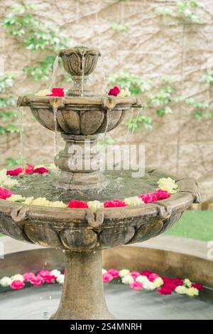 Fontaine en pierre rustique avec fleurs flottantes dans un jardin serein. Banque D'Images