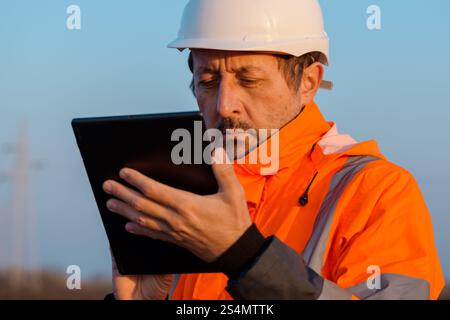 Ingénieur électricien utilisant la tablette numérique sur le terrain à proximité des pylônes électriques, mise au point sélective Banque D'Images