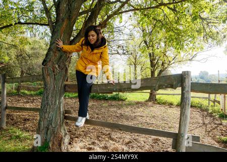 Femme en veste jaune se relaxant sur une clôture en bois dans la forêt Banque D'Images