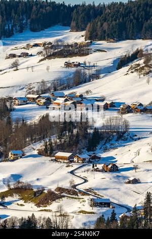 Village alpin, Autriche en hiver, enneigé éparpillé dans la vallée avec des montagnes, dans la vallée est une collection de fermes entre les forêts Banque D'Images