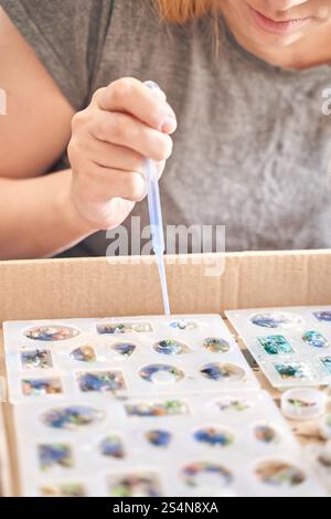 Jeune femme caucasienne fabriquant des bijoux en résine de bricolage à l'aide de moules en silicone et d'une pipette. Banque D'Images