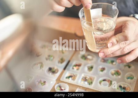 Gros plan des mains remuant la résine avec des moules pour l'artisanat de bijoux et de décorations dans l'atelier créatif. Banque D'Images