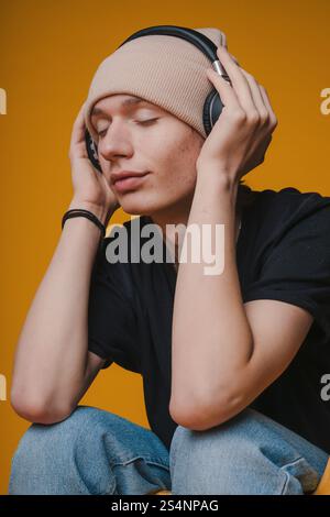 Un jeune homme profitant de sa musique préférée avec des écouteurs, sur un fond jaune vif Banque D'Images
