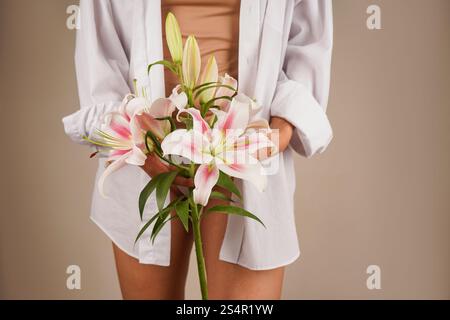 Une scène délicate de mains tenant doucement un bouquet de lis roses. La chemise blanche du modèle rehausse l'ambiance tranquille. Le bouquet repose près du Banque D'Images