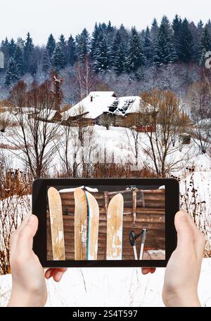 Travel Concept - office prend photo de deux paires de skis dans l'échelle de village en hiver jour sur smartphone, Russie Banque D'Images