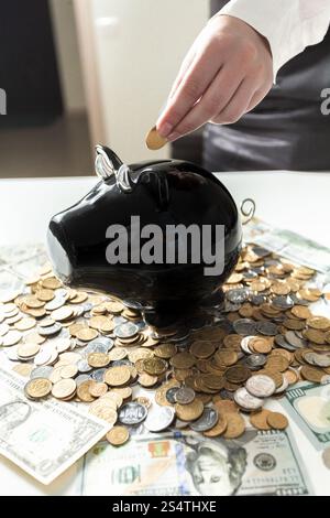 Young businesswoman putting coins in piggy bank noir Banque D'Images