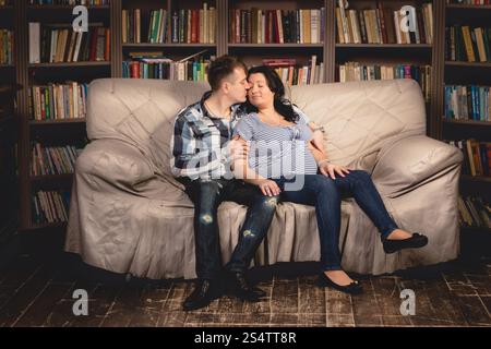 De belles jeunes femmes enceintes couple sitting on sofa contre étagères Banque D'Images