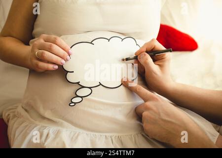 Gros plan de la photo de l'homme écrivant sur le signe de papier sur l'abdomen enceinte de wifes Banque D'Images