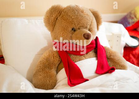 Photo gros plan de l'ours en peluche brun en écharpe rouge au lit Banque D'Images