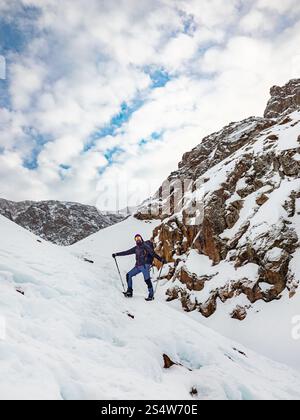 Un randonneur mâle haut dans les montagnes en hiver. Voyageur barbu avec un sac à dos debout sur une pente enneigée. Randonnée dans les montagnes d'hiver Banque D'Images
