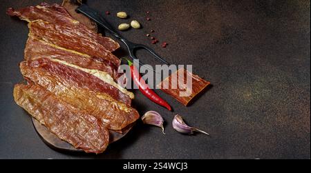 Viande salée, probablement saccadée, disposée sur une surface sombre avec un espace de copie. Banque D'Images