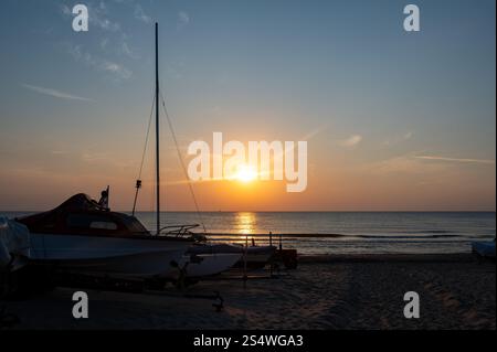 Les voiliers se trouvent sur la plage de sable, avec un beau coucher de soleil orange sur la mer Banque D'Images