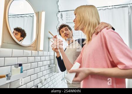 Dans une salle de bain cosy, un couple gay profite d’un moment ludique tout en préparant leur journée ensemble. Banque D'Images