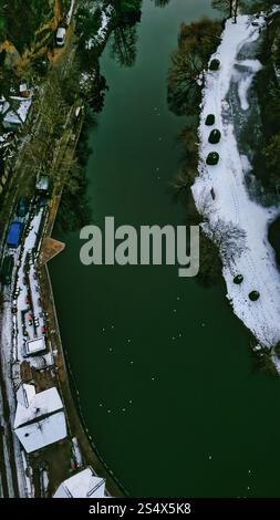 Vue aérienne d'une rive vert foncé en hiver. La neige recouvre le sol, contrastant avec l'eau vert foncé. Les bâtiments et les véhicules sont visibles le long de o Banque D'Images