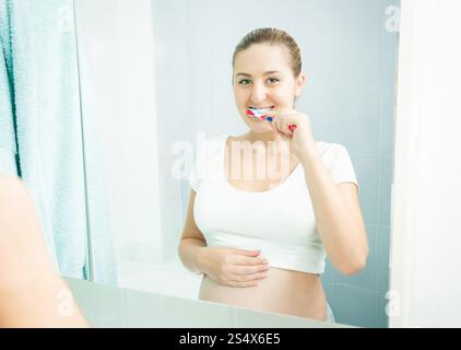 Portrait de jeune femme enceinte se brosser les dents à bains Banque D'Images