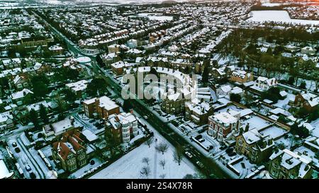 Vue aérienne d'un quartier résidentiel enneigé. Les maisons sont densément remplies, avec des rues courbes et des espaces verts visibles. L'image montre un mélange de h. Banque D'Images