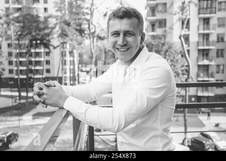 Portrait noir et blanc de l'homme souriant élégant en chemise blanche posant sur le balcon sur fond urbain Banque D'Images