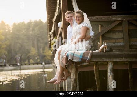 Mariée souriante heureuse et mariée se relaxant sur la jetée en bois sur le lac à la forêt Banque D'Images