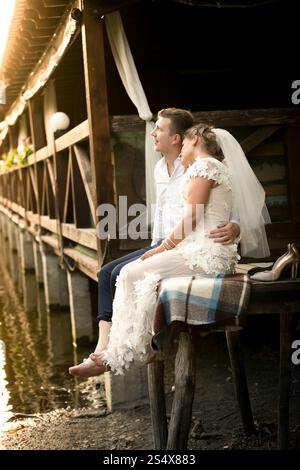 Jeune couple juste marié se relaxant sur la vieille jetée en bois au coucher du soleil Banque D'Images
